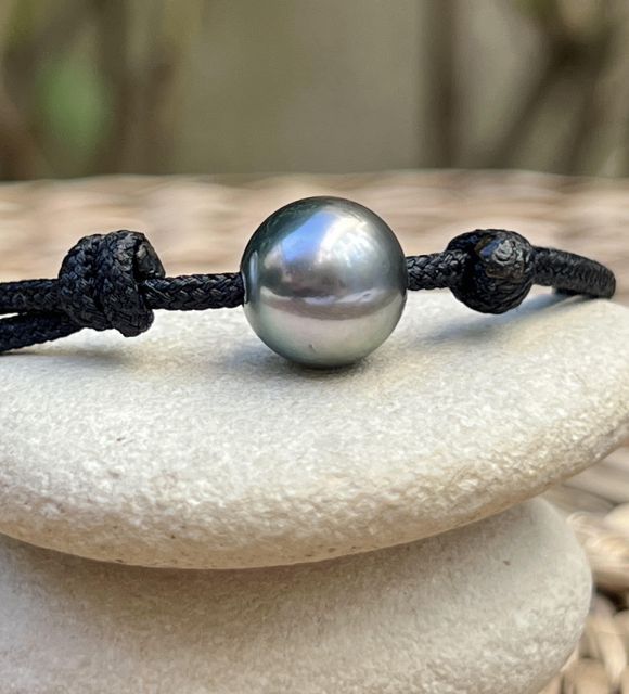 A Tahitian pearl measuring 11.30 mm, with a round shape and iridescent grey colour featuring green and pink overtones, classified as AA+ with a brilliant lustre, is showcased on an adjustable black macramé cord.