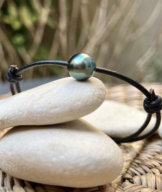 Schwarzes Lederarmband mit verstellbaren Knoten, verziert mit einer runden Tahiti-Zuchtperle (10,79 mm, Qualität AA) in Pfauenfarbe mit sehr hohem Glanz.