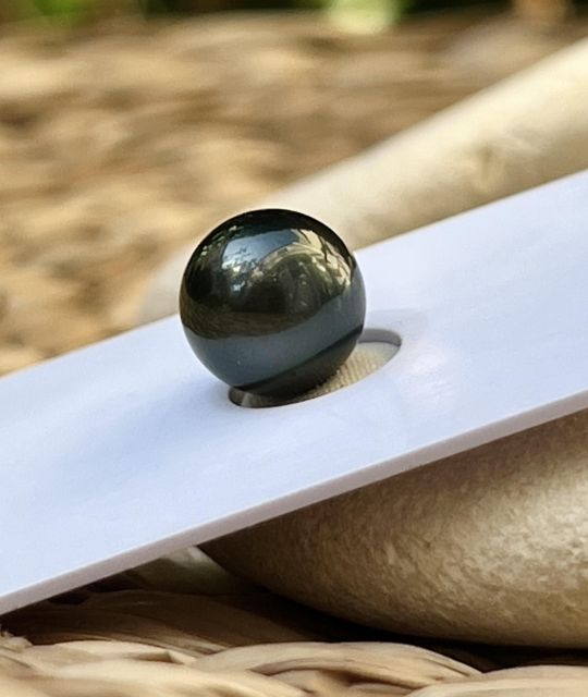 Perle de Tahiti ronde de 10,26 mm, noire sublimée par un orient vert foncé qui lui confère un aspect presque laqué - livraison gratuite en Union Européenne