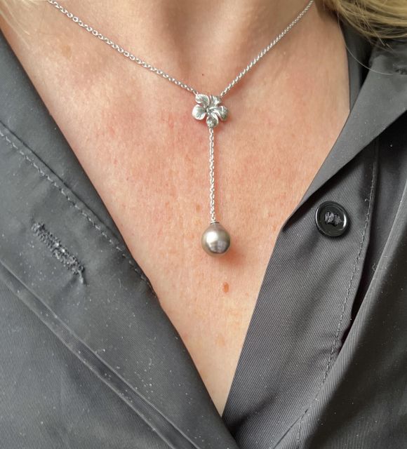 首元に咲く花。それは細かに彫刻されたハイビスカスで、捧げ物のように置かれ、光がユニークなタヒチ真珠に届く。