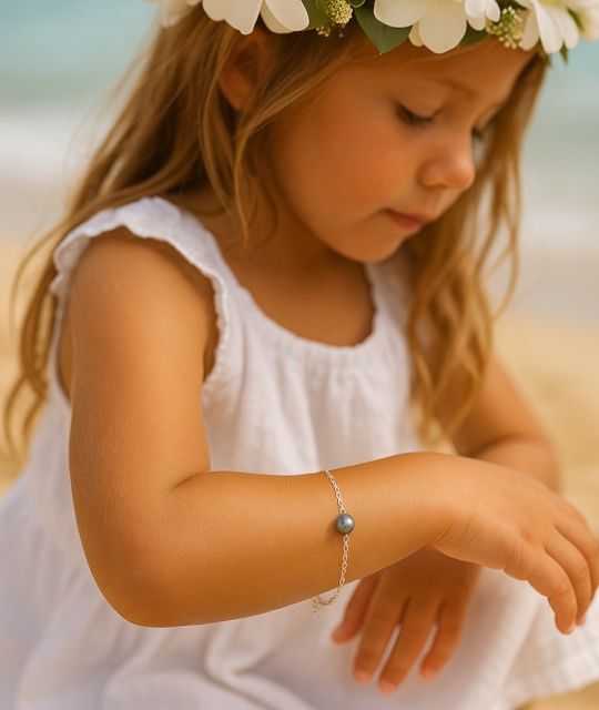 Une perle de Tahiti semi-baroque, de qualité A, comme un éclat venu du lagon, posée sur une chaîne d’argent pour accompagner les premiers instants de la vie.