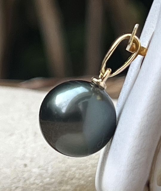 Suspendue à une bélière en or jaune 18 carats, cette perle d’exception révèle, sous certains rayons du soleil, de magnifiques reflets bleus, typiques des perles de Tahiti