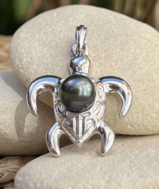 Eine silberne Schildkröte mit Marquesas-Motiven, Symbol für Schutz und Langlebigkeit, beherbergt eine Tahiti-Perle in Tropfenform mit 8,64 mm Durchmesser, in schimmerndem Pfauenblau.