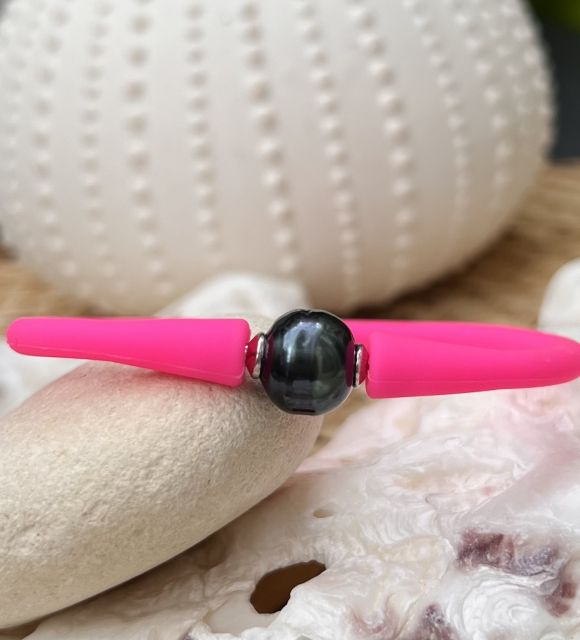 Un brillante braccialetto in silicone rosa fluorescente ornato con una scura perla nera di Tahiti