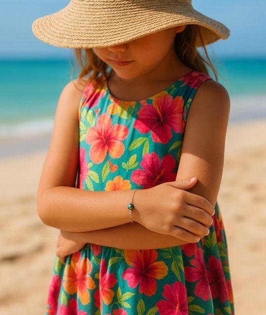 Ein vergoldetes Kinderarmband. Peacock-Schimmer, schwarz oder sanftes Grau, um die ersten Gesten eines Lebens im Licht zu erhellen.