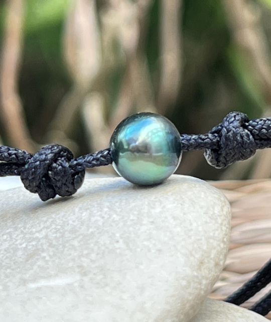 Eine runde Tahiti-Zuchtperle mit einem Durchmesser von 9,09 mm, in Lagunenfarbe mit blauen und grünen Schimmern, in AA-Qualität und mit ausgezeichnetem Glanz, zeigt sich auf einem verstellbaren schwarzen Makramee-Band.