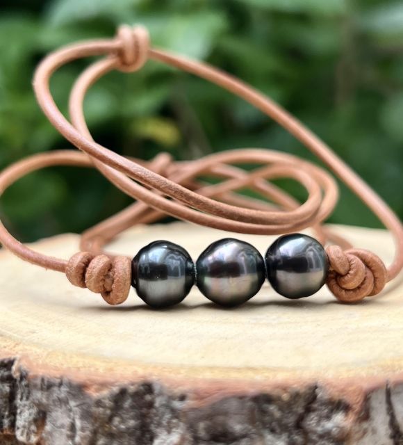 3 perles de Tahiti peacock sur un cuir marron. Leur éclat profond raconte les fonds du lagon, leurs reflets dansent comme des braises sous la lune