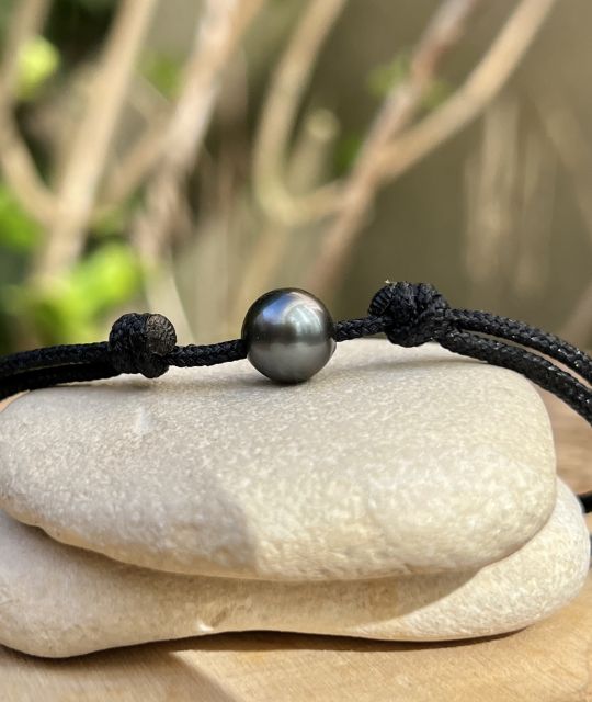 Eine runde Tahiti-Perle von 8,88 mm, grau mit einem glänzenden Schimmer, offenbart ihre Echtheit an einem verstellbaren schwarzen Band - kostenlose Lieferung innerhalb der EU.