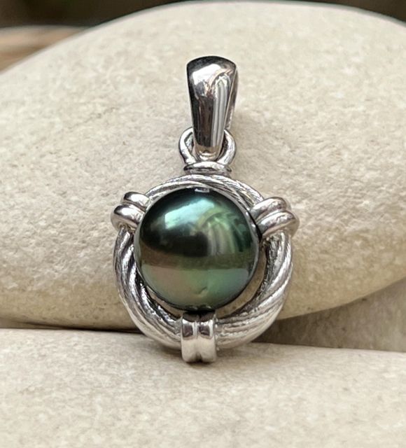 Un bijou masculin, sobre et puissant. En argent rhodié, il accueille une perle de Tahiti ronde (9/10 mm), qualité AA, au lustre intense et aux reflets peacock, noirs ou gris.