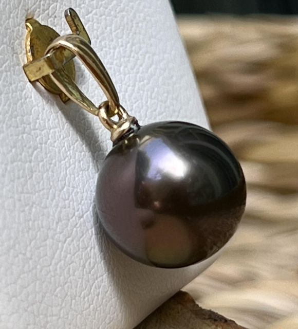 Откройте для себя Aura, подвеску из 18-каратного золота, украшенную настоящей чернильно-пурпурной жемчужиной Таити AAA+ диаметром 11,03 мм с исключительным блеском. Светящееся и утонченное ювелирное творение, подписанное Poemotu.