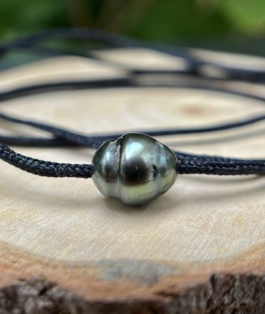 Ein tiefes Schimmern, wechselnde Reflexe, ein lebendiger Glanz. Reva umschließt den Hals mit einem rohen Hauch, dem einer halbbarocken Tahitiperle in schimmernden Pfauenfarben.