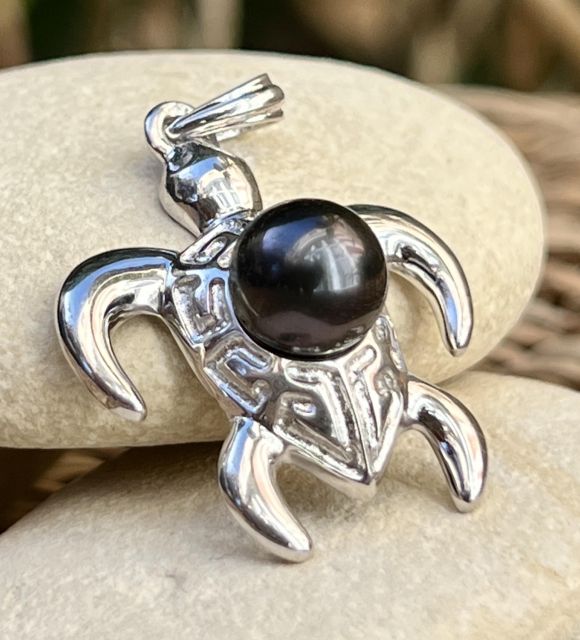 Une tortue en argent aux motifs marquisiens, symbole de protection et d’équilibre, abrite une perle noire de Tahiti ronde de 8,92 mm, voilée de prune et au lustre excellent