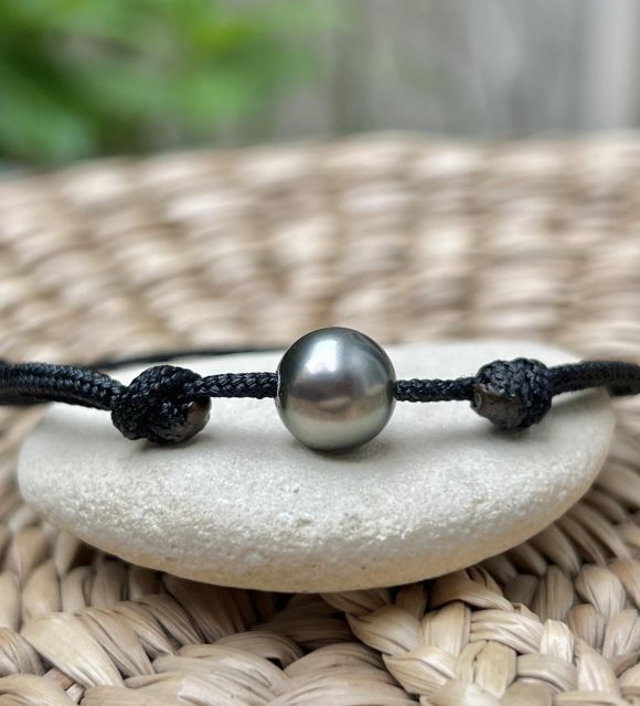 Sur un lien noir profond, discret et intemporel, se pose une perle de Tahiti de forme ronde, à la couleur peacock bleue rare et captivante - certifié et Garanti