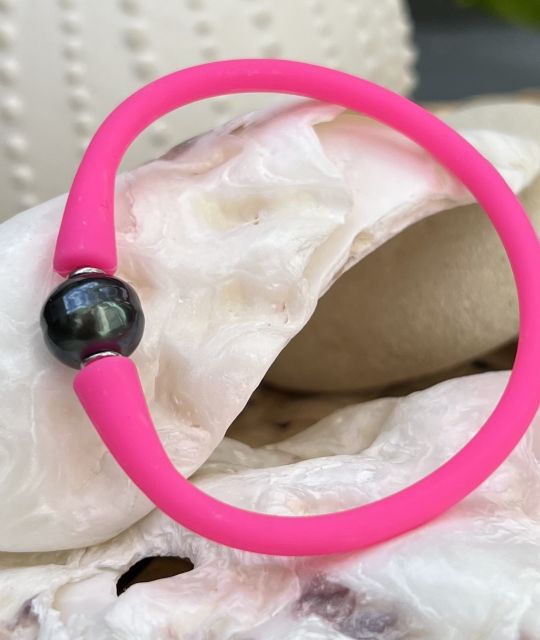 Ein strahlendes Armband aus neonrosa Silikon, verziert mit einer dunklen schwarzen Tahitiperle