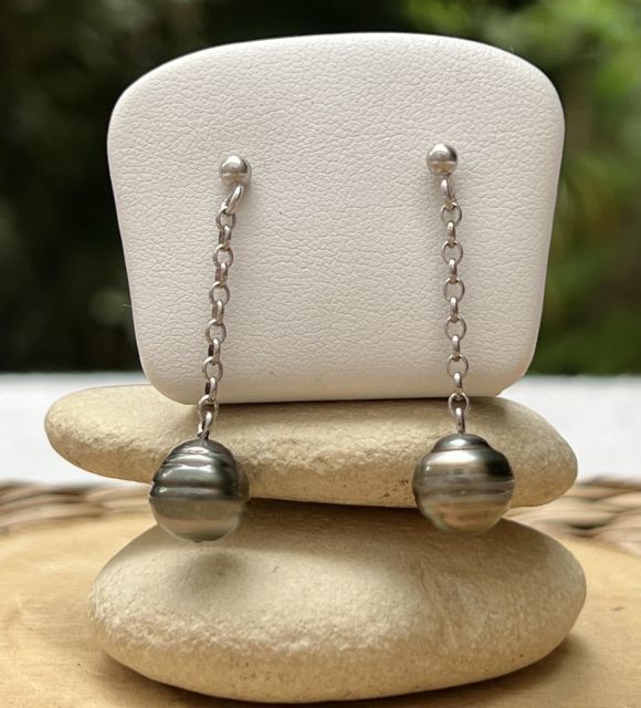 2 perles de Tahiti grises, comme deux éclats de lagon glissant le long d’un fil d’argent. Légères et lumineuses, elles dessinent la grâce à chaque mouvement.