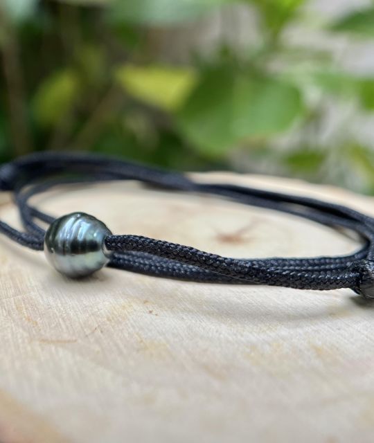 Eine Tahiti-Perle in Grau-Blau, wie von den Wellen geformt, ruht im Zentrum des Halsreifs. Tiefer Glanz, wechselnder Schimmer, rohe Präsenz.